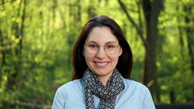 An attractive young brunette ecologist botanist woman with glasses smiles and looks at the camera in the forest and smile. Caring for nature.