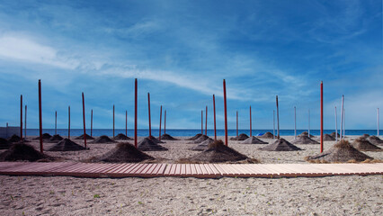 Abgeh&auml;ngte Strohschirme am Strand , im Vordergrund Laufsteg