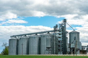 silver silos on agro manufacturing plant for processing drying cleaning and storage of agricultural products, flour, cereals and grain. Large iron barrels of grain. Granary elevator