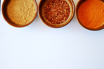 turmeric, chili and galgant spice powder in brown bowls on white background with space for text