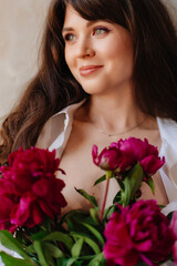 a beautiful young brunette woman in a white shirt with a bouquet of peonies.