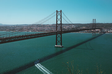 25 de Abril Bridge famous place Lisbon in Portugal. Red bridge, river, boat and cityscape