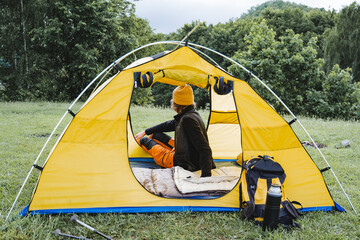 Summer camping in a tent, a person sitting in a campsite and enjoying nature, a yellow tourist...