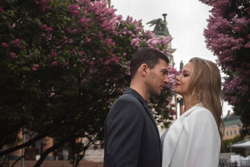 Obraz premium date, a young couple, a man and a woman walking in the city among blooming lilacs