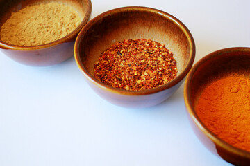 turmeric ginger and chili spices in brown bowls on white background with space for text, three different cooking spices on white background