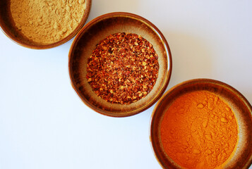 directly above shot of chili, turmeric and galgant powder spices in brown bowls on a white background with space for text, top view on different cooking spices in bowls