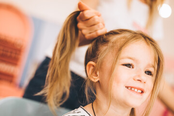 Fototapeta premium Stylish little girl in a beauty salon for children where she made a beautiful hairstyle. Female stylist makes stylish hairstyle to little girl.