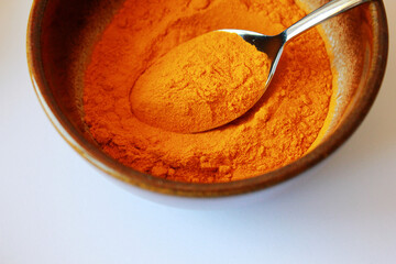 yellow turmeric powder in a brown bowl with a spoon on white background, turmeric powder as ingredient for cooking