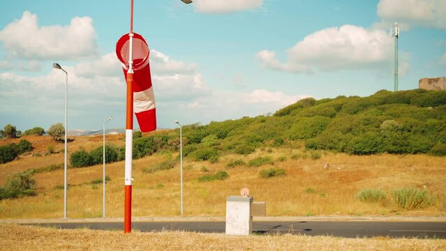 Wind sock fly. Summer hot day on private sporty airport with abandoned windsock, wind is blowing and windsock is lazy moving. Windsock with cloud sky mountain and road with cars on background 