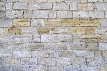 An old damaged wall made of white, gray and yellow bricks as a background