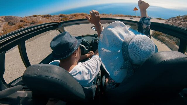 Party couple on honeymoon driving in convertible car without roof on mountain road in Santorini island at Ancient Thera, Greece. Wide angle lens shot.