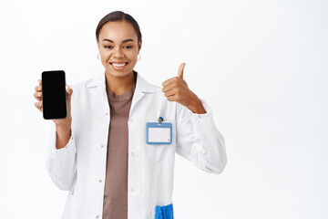 Woman doctor shows thumbs up and smartphone screen app, mobile healthcare application interface,...