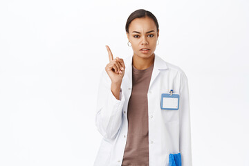 Doctor shaking finger in disapproval, prohibit something to patient, standing over white studio...