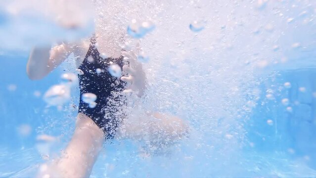 Girl with swimsuit swimming on a blue water pool with underwater rising bubbles, slow motion