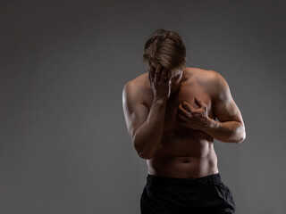 Obraz premium A muscular man expressively emotionally poses on a gray background. Screams and suffers. The guy is an athlete with pumped-up muscles. beautiful body relief.