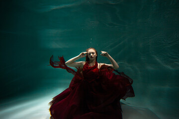 Underwater shooting, a beautiful young woman in a red dress is swimming under the surface of the...