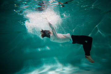 Beautiful underwater shooting, guy in white shirt and pants has fallen under the water and drowning. go to bottom, concept. young man paddles with his hands under water, waves and splashes around him