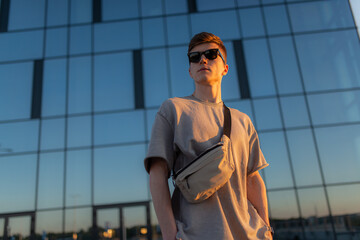 Portrait of handsome tourist hipster man in sunglasses with bag handy, standing guy near the building in downtown. Calm relaxing moment, summer vacation concept - 514533103