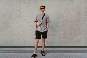 Portrait of handsome confident stylish hipster man in sunglasses with bag handy, standing guy near the concrete wall. Calm relaxing moment, summer vacation concept - 514533122