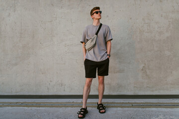 Portrait of handsome confident stylish hipster man in sunglasses with bag handy, standing guy near the concrete wall. Calm relaxing moment, summer vacation concept - 514533130