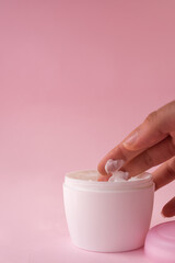 Hand taking cream from a skin cream bottle for women on pink background