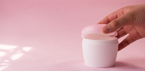 Hand opening a skin cream bottle for women on pink background