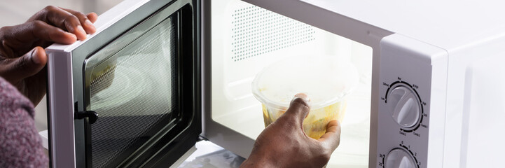 Man's Hand Heating Food In Microwave Oven