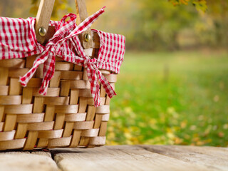 A cozy straw picnic basket on a wooden table against the backdrop of autumn nature, golden leaves...