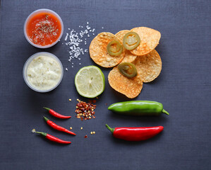 Fototapeta na wymiar Mexican cuisine ingredients including nachos corn jalapeno peppers chilli peppers lemon slices salsa and sour cream 