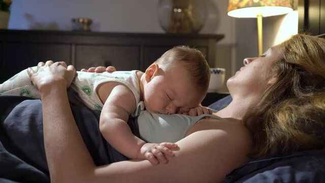 A tired mother sleeping together with his baby son on her chest in bedroom. Family bonding. Motherhood