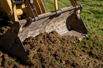 Clearing and leveling a private land plot. Yellow excavator driving earth in a wide bucket - obrazy, fototapety, plakaty