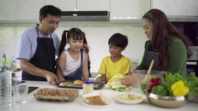 Asian families cook together on weekends. Happy families are helping each other make salads. Bake the bakery by looking at the recipes from the tablets in the kitchen. Family and teamwork concept