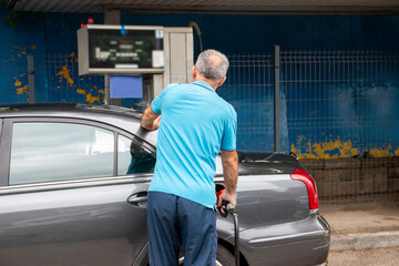 Mature man pouring petrol into tank of his vehicle on filling station. Travel,transportation and...