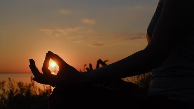 Close up hand of woman exercising yoga lotus pose at sunset. Hands contour in mudra position on setting sun background.
