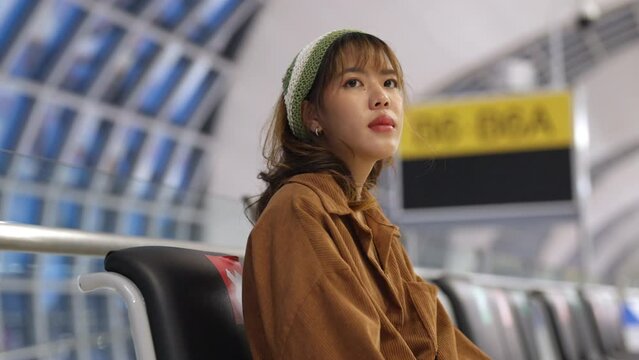 4K Young Asian woman passengers using mobile phone while waiting for flight at boarding gate in airport terminal. Attractive female traveler go to travel destination by airplane on holiday vacation