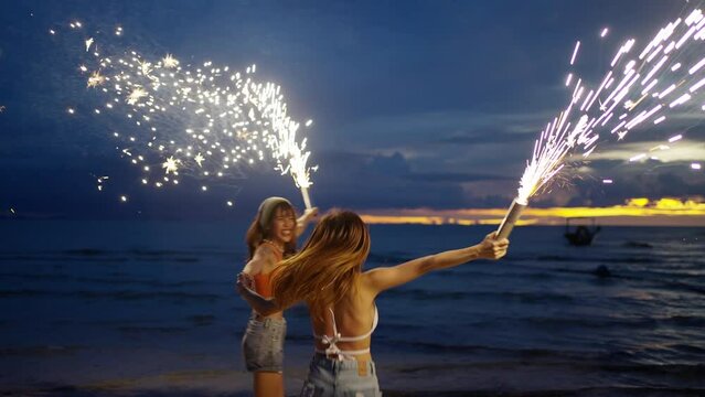 4K Young Asian woman having fun dancing and playing sparklers together on tropical island beach in summer night. Happy female friends enjoy outdoor lifestyle nightlife on holiday travel vacation trip