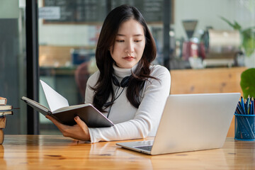 Beautiful Asian female college student studying online on laptop computer. Searching the web for information on studying concepts, studying, working at a coffee shop.