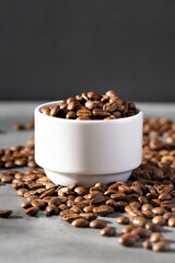 Roasted coffee beans in a white mug, coffee beans scattered around. 