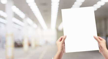 Hands holding white empty paper at factory production background.