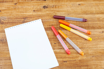 felt-tip pens and an empty notepad lie on a wooden table