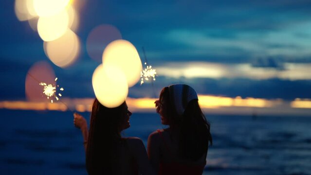 4K Group of Young beautiful Asian woman sitting and playing sparklers together on tropical island beach at summer night. Happy female friends enjoy and fun outdoor lifestyle on holiday travel vacation