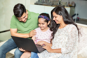 Young Indian parents teach daughter how to use laptop computer at home. Asian girl child study online education, english lesson. tell story.