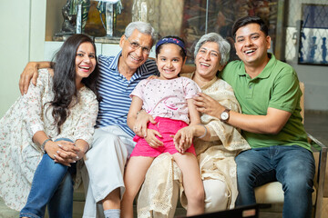 Portrait of happy indian family sitting on sofa at home, Asian grandparents and young parents with...