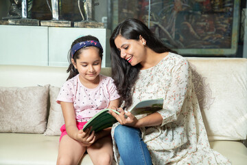 Young indian mother helping little daughter with study at home, Asian girl child with notebook doing homework with her mom. 