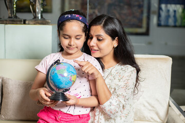 Young indian mother teaching daughter use of globe, Asian teacher and girl child studying geography.