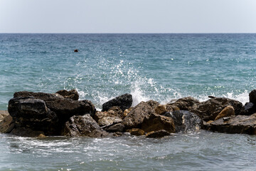 Beach on the Italian Riviera with sun, sea and stones in the sea water. Rough Sea and Foamy Waves on Shore at Mediterranean Coast in Sunrise