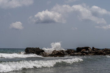 Beach on the Italian Riviera with sun, sea and stones in the sea water. Rough Sea and Foamy Waves on Shore at Mediterranean Coast in Sunrise