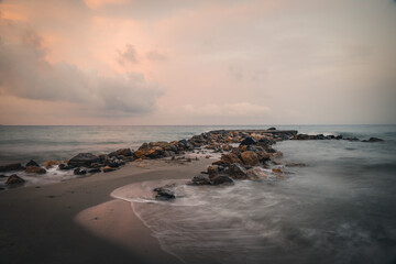 Beach on the Italian Riviera with sun, sea and stones in the sea water. Rough Sea and Foamy Waves on Shore at Mediterranean Coast in Sunrise