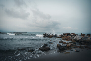 Beach on the Italian Riviera with sun, sea and stones in the sea water. Rough Sea and Foamy Waves on Shore at Mediterranean Coast in Sunrise