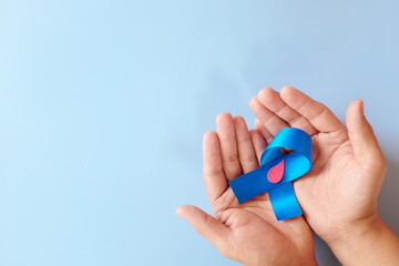 Top view of hand holding blue ribbon with red blood drop and copy space. World diabetes day concept.